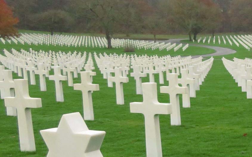 Rows of white cross grave markers in a military cemetery stretching across a green landscape.